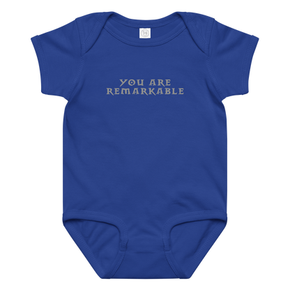 "You are remarkable" printed on a royal baby jersey bodysuit laying on a flat surface amongst other clothes