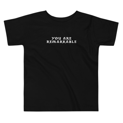 "You are remarkable" printed on a black toddler short sleeve tee laying on a flat surface
