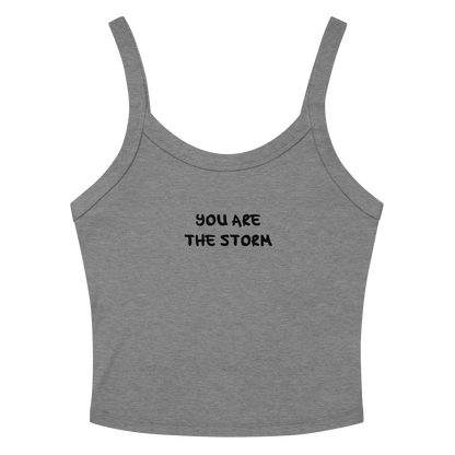 "You are the storm" printed on a athletic heather women's micro-rib tanktop laying on a flat surface amongst sunglasses and shorts
