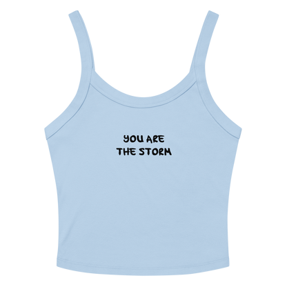 "You are the storm" printed on a solid baby blue blend women's micro-rib tanktop laying on a flat surface amongst sunglasses and shorts