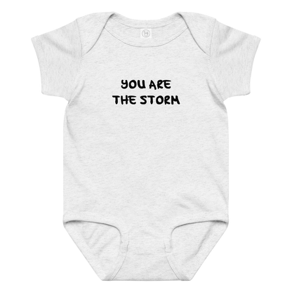 "You are the storm" printed on a ash baby jersey bodysuit laying on a flat surface amongst other clothes