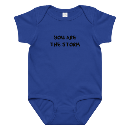 "You are the storm" printed on a royal baby jersey bodysuit laying on a flat surface amongst other clothes