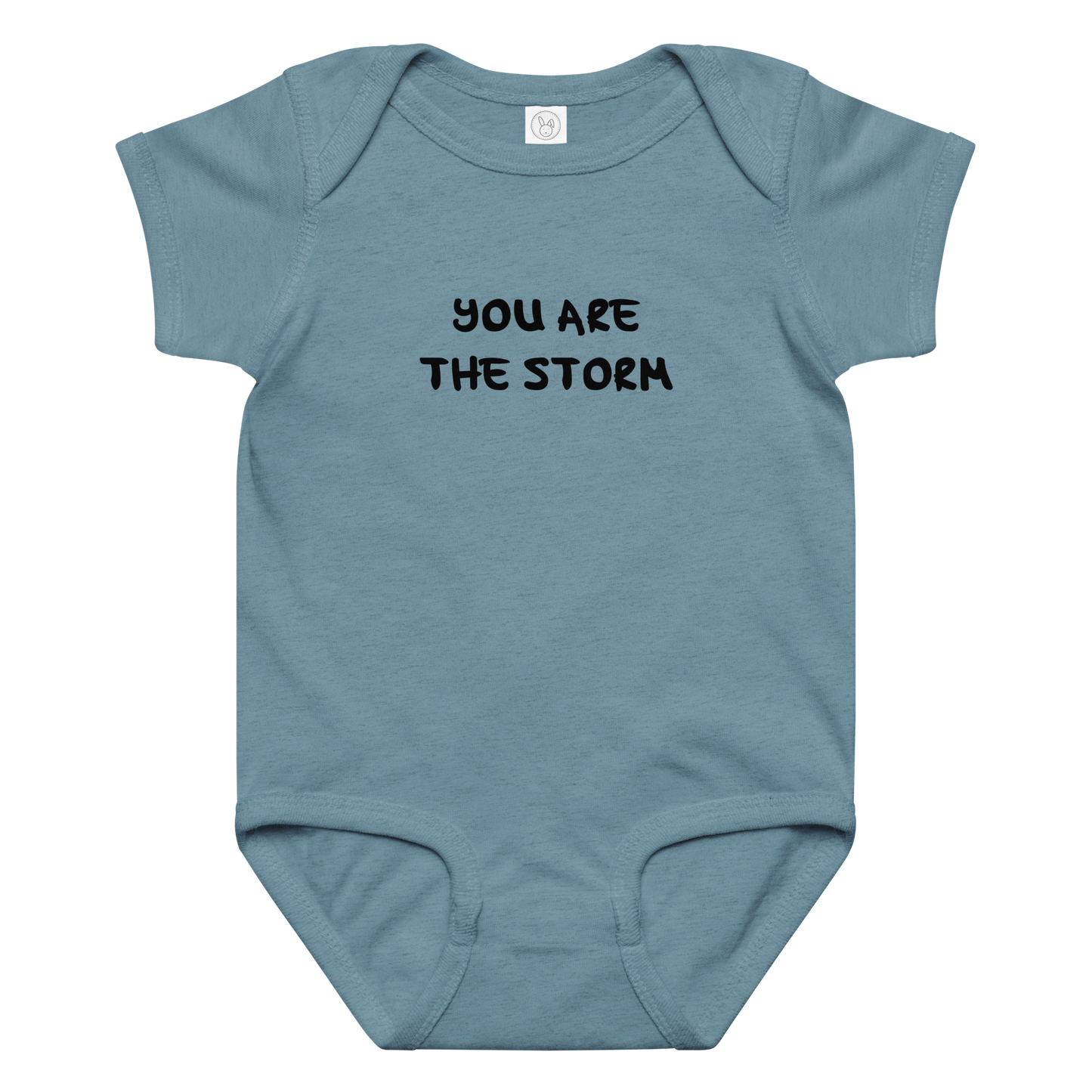 "You are the storm" printed on a vintage indigo baby jersey bodysuit laying on a flat surface amongst other clothes
