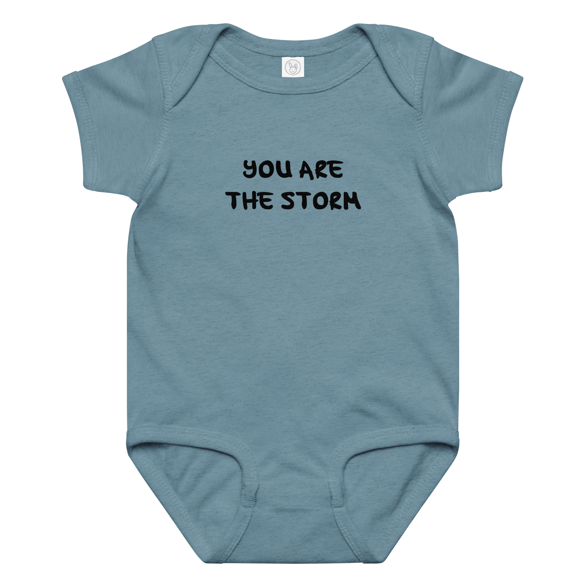 "You are the storm" printed on a vintage indigo baby jersey bodysuit laying on a flat surface amongst other clothes