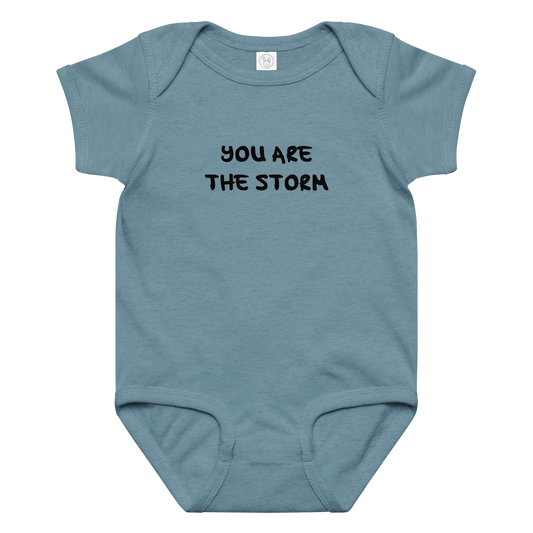 "You are the storm" printed on a vintage indigo baby jersey bodysuit laying on a flat surface amongst other clothes