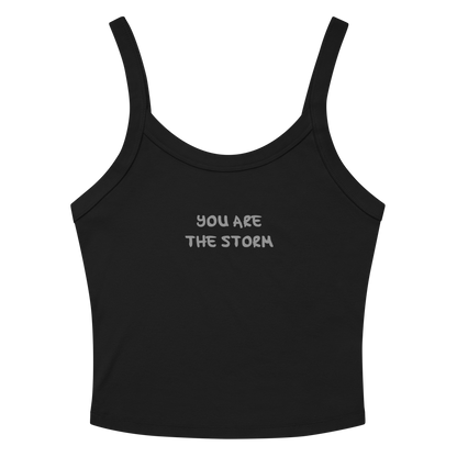 "You are the storm" printed on a solid black blend women's micro-rib tanktop laying on a flat surface amongst sunglasses and shorts