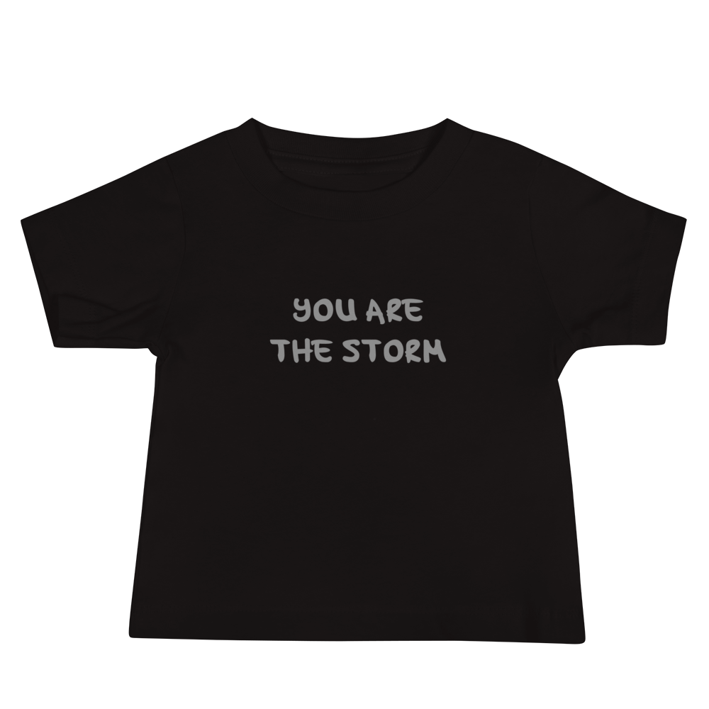 "You are the storm" printed on a black baby jersey short sleeve tee laying on a flat surface