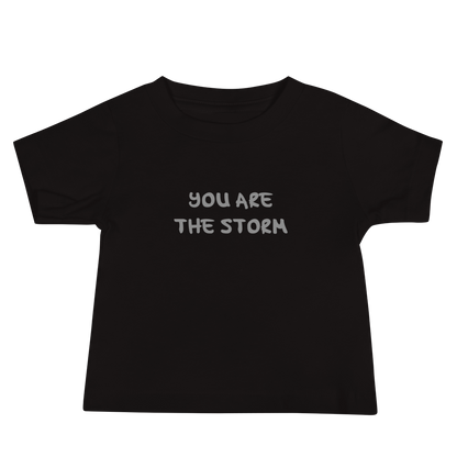 "You are the storm" printed on a black baby jersey short sleeve tee laying on a flat surface