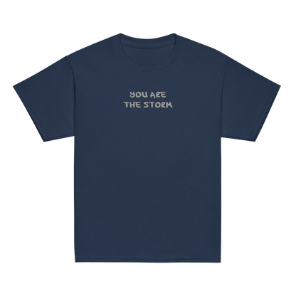 "You are the storm" printed on a navy youth classic tee laying on a flat surface