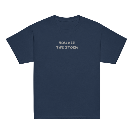 "You are the storm" printed on a navy youth classic tee laying on a flat surface