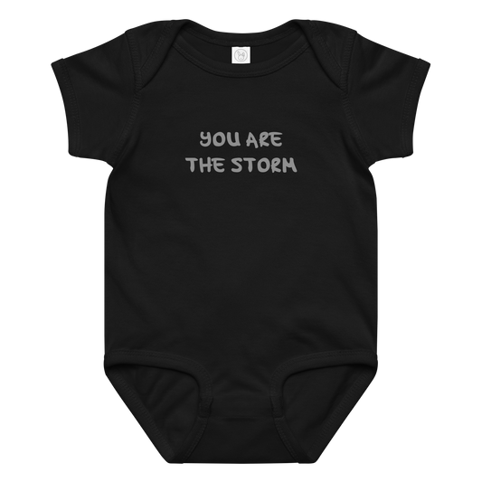 "You are the storm" printed on a black baby jersey bodysuit laying on a flat surface amongst other clothes