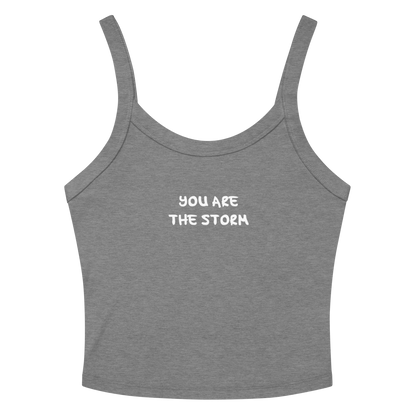 "You are the storm" printed on a athletic heather women's micro-rib tanktop laying on a flat surface amongst sunglasses and shorts
