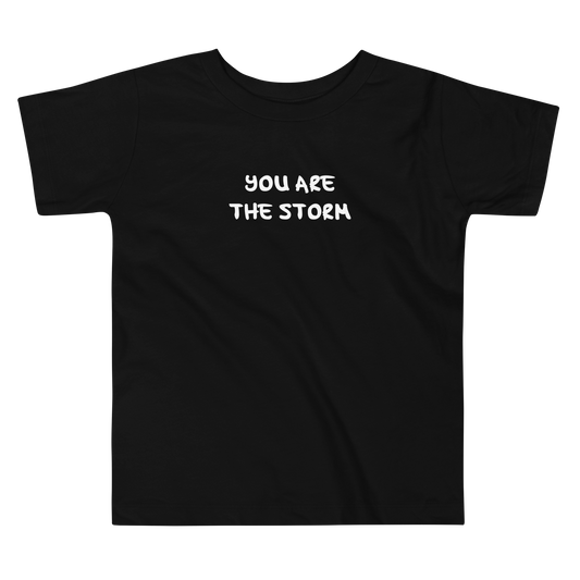 "You are the storm" printed on a black toddler short sleeve tee laying on a flat surface