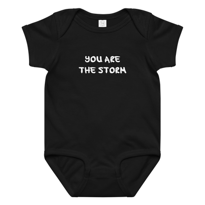 "You are the storm" printed on a black baby jersey bodysuit laying on a flat surface amongst other clothes