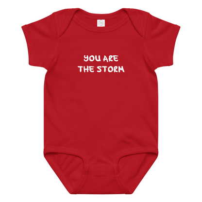"You are the storm" printed on a red baby jersey bodysuit laying on a flat surface amongst other clothes