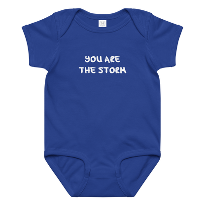 "You are the storm" printed on a royal baby jersey bodysuit laying on a flat surface amongst other clothes