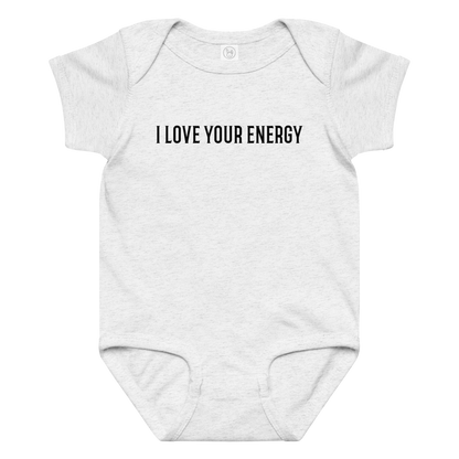 "I love your energy" printed on a ash baby jersey bodysuit laying on a flat surface amongst other clothes